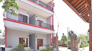 A multi-story building with balconies, a gated entrance, and a small garden area. - RedDoorz @ Uluwatu Bali (Pecatu)