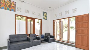 Eine großzügige Lobby mit einem grauen Ecksofa, einem kleinen Tisch und zwei Sesseln. Holzrahmenfenster und eine Glastür führen nach draußen.