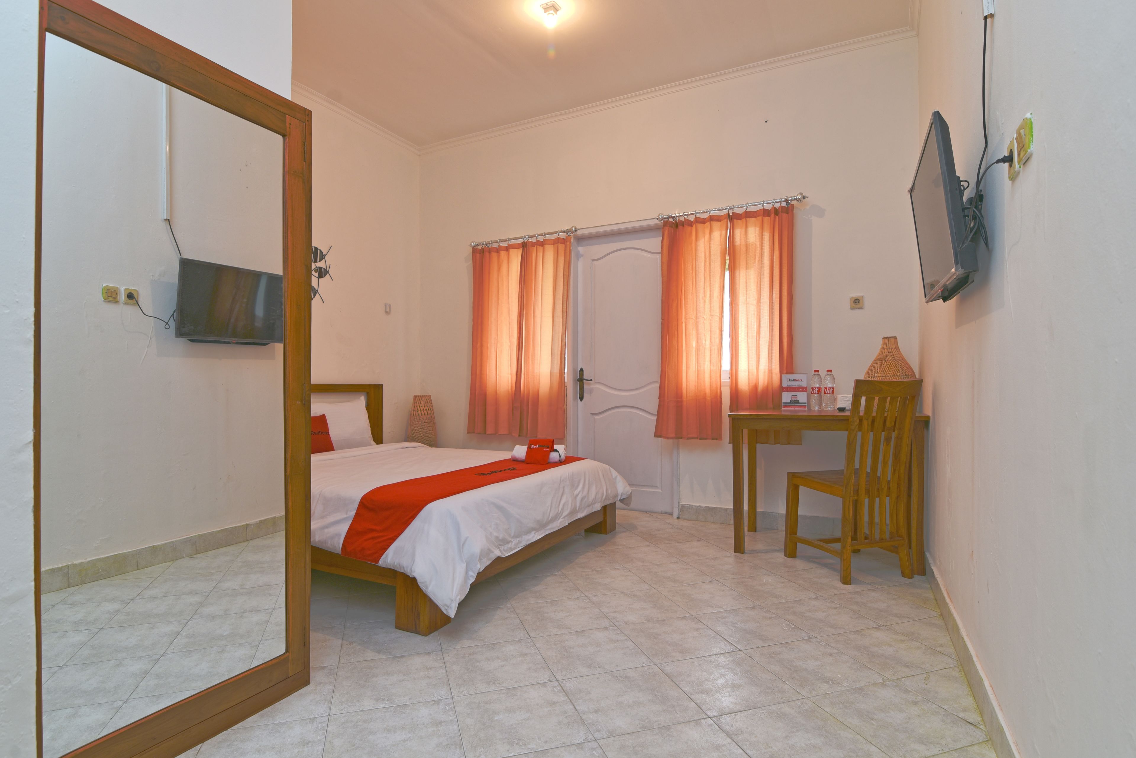A bedroom with a bed, a desk, a chair, a television, and a door with curtains.