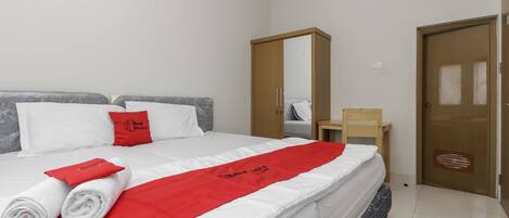 Una cama bien hecha con ropa de cama blanca y roja, un armario de madera, una mesita de madera y una puerta con mirilla.
