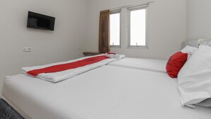 A hotel room with a bed, a TV mounted on the wall, and two windows with curtains. - RedDoorz near Central Park Mall (Jakarta)