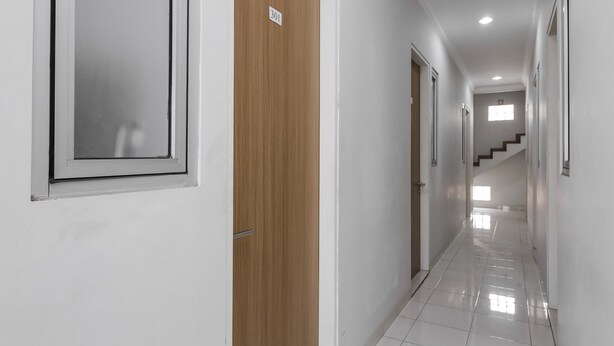 A clean, well-lit hallway with white walls, a wooden door, and a number sign. - RedDoorz near Central Park Mall (Jakarta)
