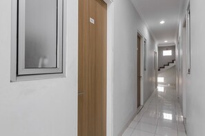 A clean, well-lit hallway with white walls, a wooden door, and a number sign. - RedDoorz near Central Park Mall (Jakarta)