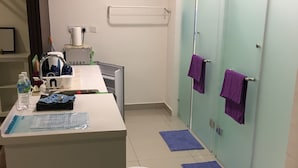 A modern bathroom with a white sink, a mirror, and a towel rack with purple towels. - 1 Bedroom Apartment @ Trefoil Setia Alam (Shah Alam)