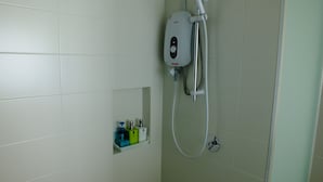 A bathroom with white tiles, a shower with a handheld showerhead, and a small shelf with toiletries. - 1 Bedroom Apartment @ Trefoil Setia Alam (Shah Alam)