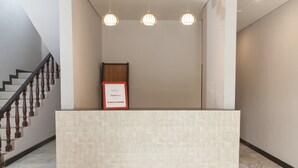 Aula, jossa on laatoitettu vastaanottotiski, kehystetty kyltti ja puukäsijohteilla varustetut portaat.