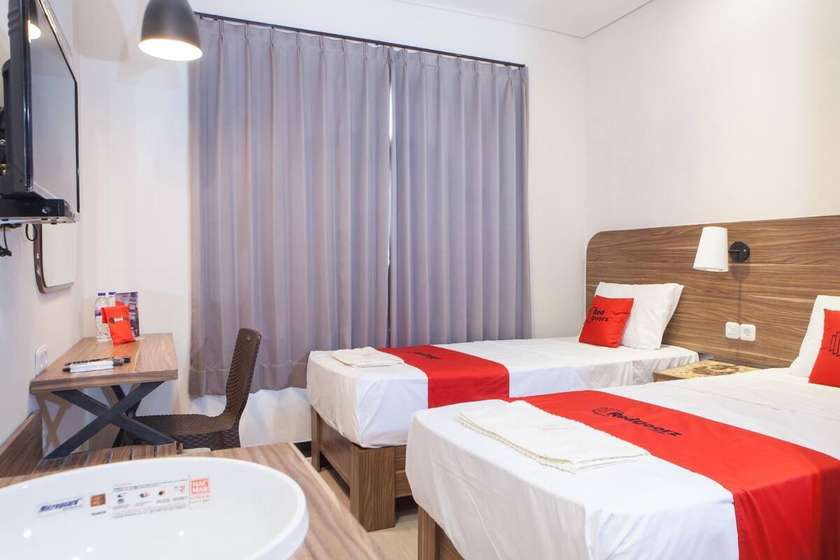 Habitación de hotel con dos camas, cabecera de madera, escritorio con silla, una mesa, televisión y ventana con cortinas.