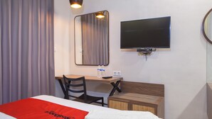 Hotellihuone, jossa on sänky, työpöytä tuolilla, televisio ja peili.