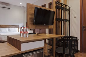Une chambre d’hôtel avec une table à manger en bois, un téléviseur fixé au mur, un lit avec une literie blanche et un petit coin cuisine.