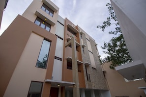 Un immeuble à plusieurs étages doté d’une architecture moderne, caractérisé par un mélange de façades en verre et en pierre, et une entrée imposante avec une porte rouge.