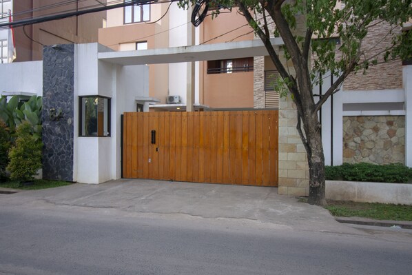 A modern residential building with a gated entrance, stone facade, and a tree in the foreground. - RedDoorz Plus @ CBD Bintaro (South Tangerang)