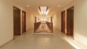 A spacious, well-lit hallway with a central staircase, flanked by wooden doors and a metal railing. - RedDoorz Plus @ CBD Bintaro (South Tangerang)