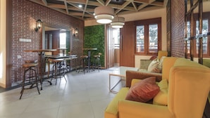 A modern interior with a brick wall, green wall, yellow sofa, and bar stools. - RedDoorz Plus @ CBD Bintaro (South Tangerang)