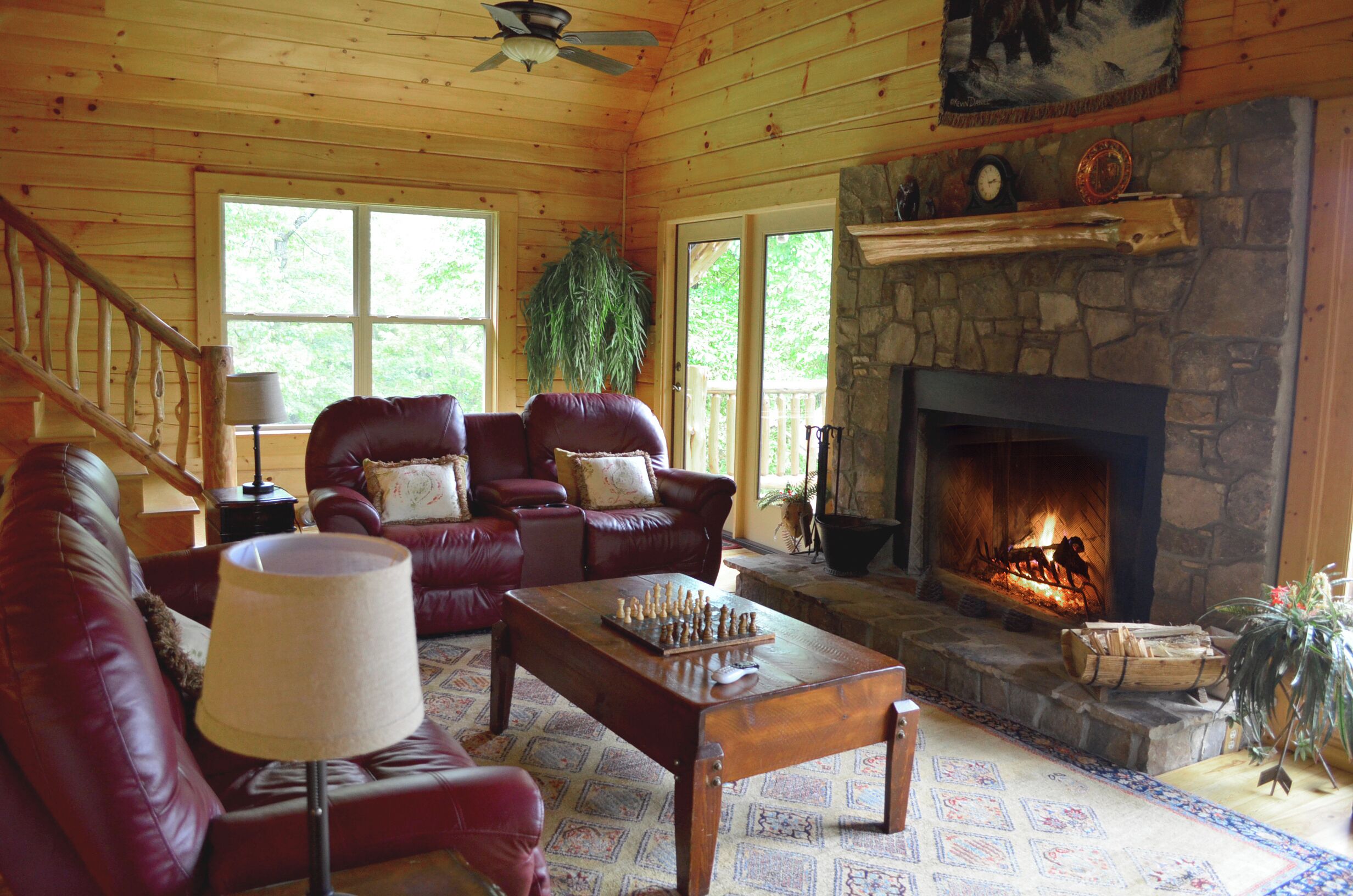 A cozy cabin interior with a stone fireplace, leather sofas, and a chessboard on a wooden table.