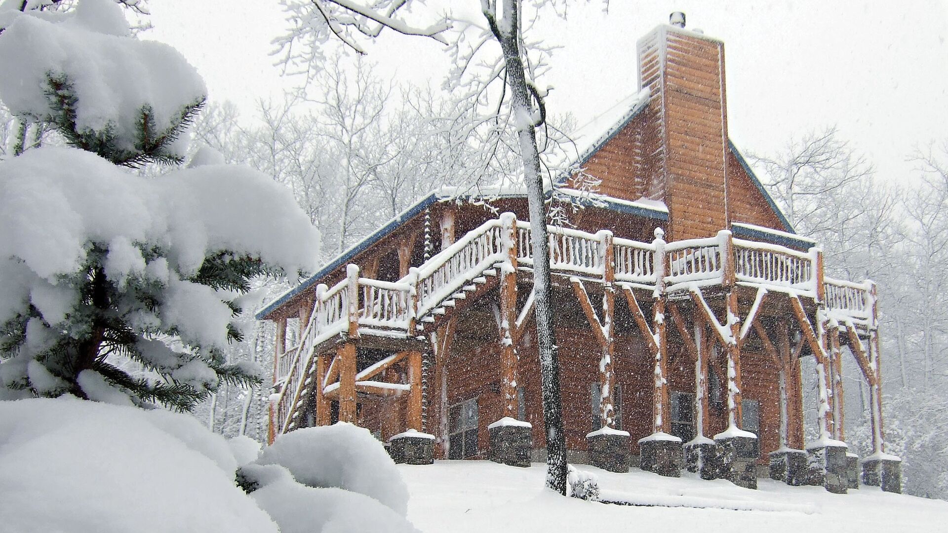 Une cabane en bois dotée d’un balcon, entourée d’arbres couverts de neige.