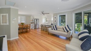 A modern kitchen with white cabinets, a stainless steel refrigerator, and a dining area with wooden chairs. - Sunny Time - Avoca Beach (Avoca)