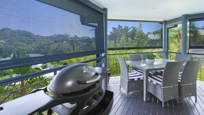 An outdoor patio with a grill, wicker furniture, and a view of a lush landscape. - Sunny Time - Avoca Beach (Avoca)