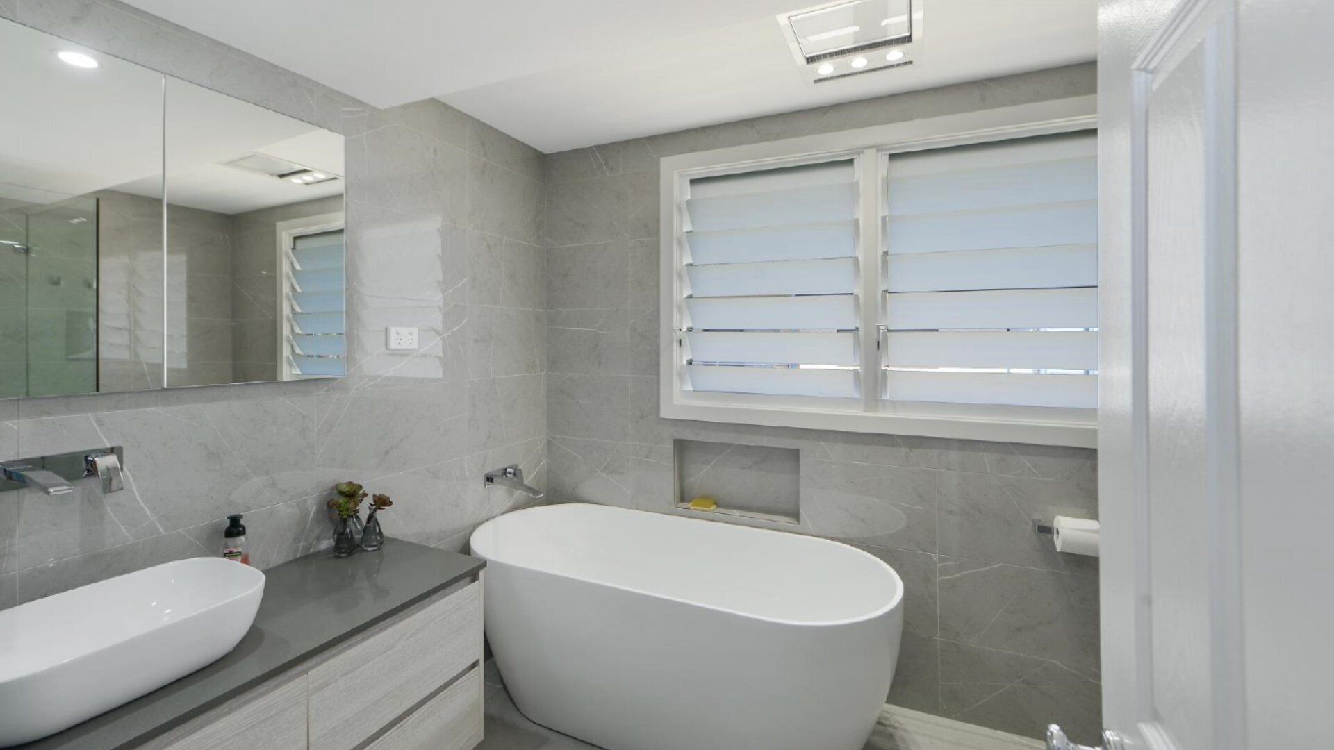 A modern bathroom with a freestanding bathtub, a double sink vanity, and a large mirror.
