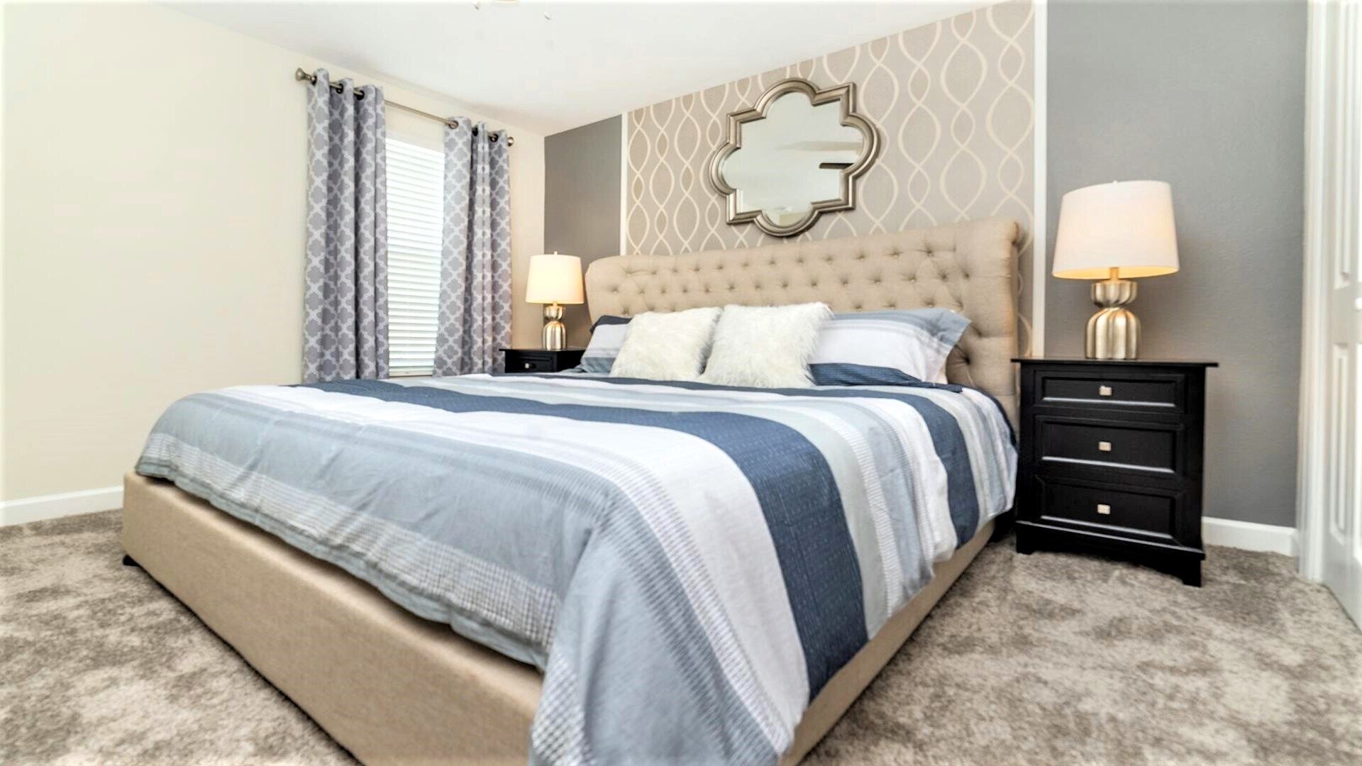 A bedroom with a large bed, two bedside tables with lamps, a decorative mirror, and a patterned wall.