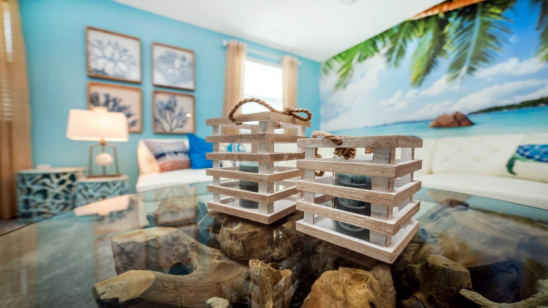 Een houten constructie op een glazen tafel, een blauwe muur met ingelijste foto’s, een witte bank en een lamp.