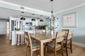 A modern kitchen with a central island, stainless steel appliances, pendant lighting, and a dining area with wooden chairs and a table.