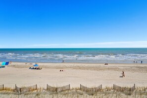 Ein Strand mit einem Holzzaun im Vordergrund, blauem Himmel und dem Meer im Hintergrund.
