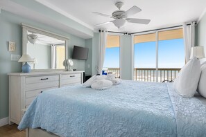 Ein Schlafzimmer mit Bett, Deckenventilator, Fernseher, Kommode und Blick auf den Strand.