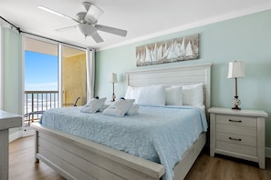 A bedroom with a bed, nightstands, a ceiling fan, a painting, and a view through a glass door.