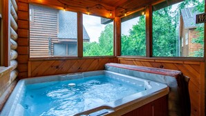 Una cabaña de madera con jacuzzi, ventanas amplias y vistas al bosque circundante.