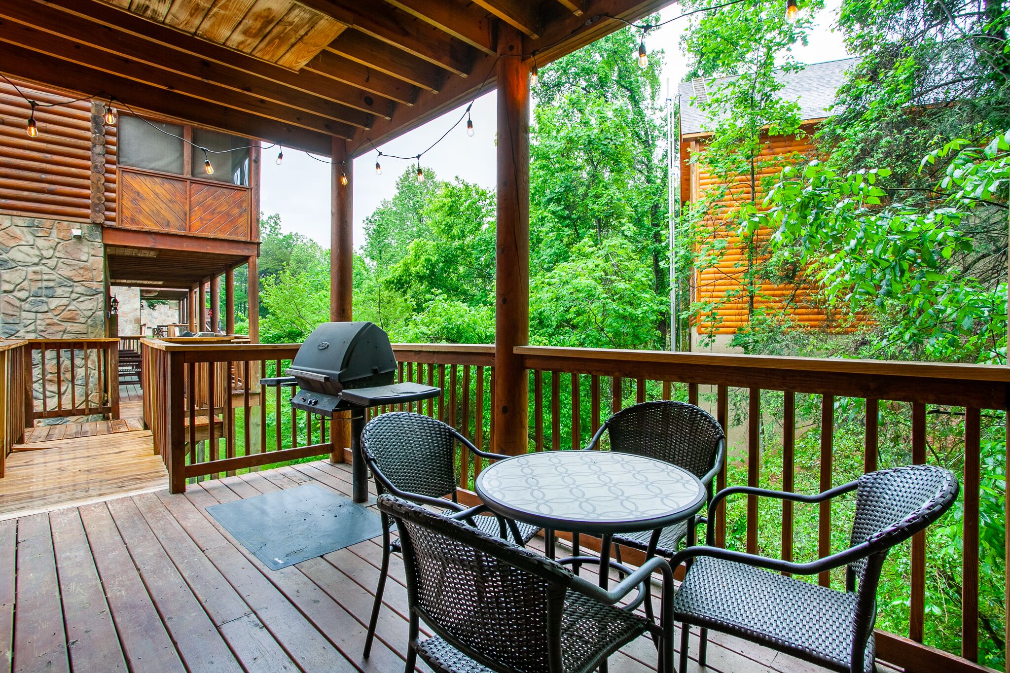 A wooden deck with a grill, outdoor seating, and a stone wall.