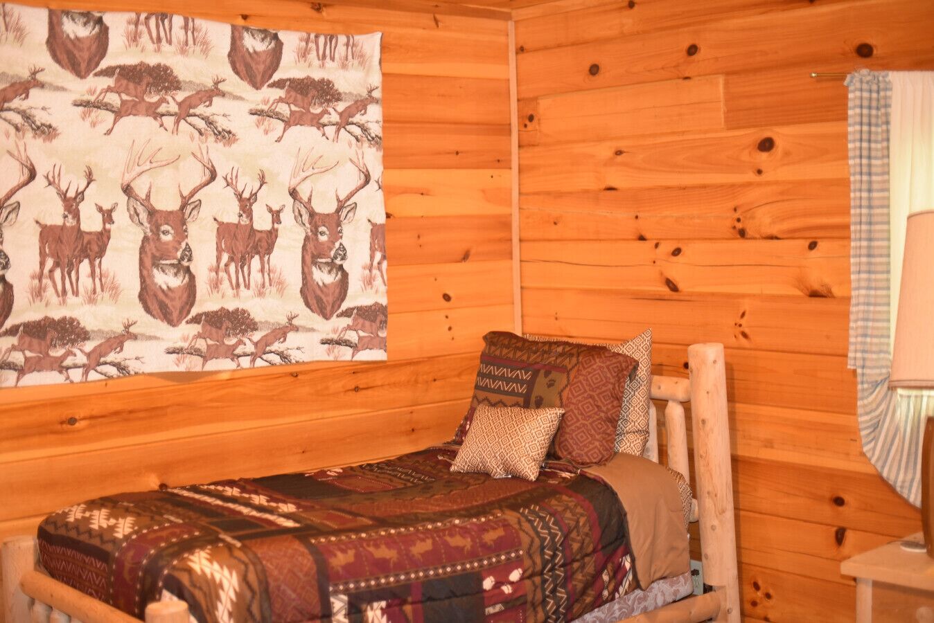 A wooden cabin room with a bed, a blanket, and a wall tapestry of deer.