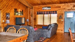 A cozy cabin interior with a wooden interior, a sofa, a television, and a dining area.