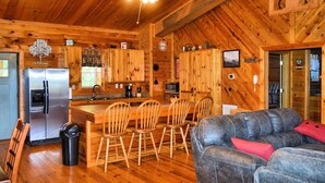 A wooden cabin interior with a kitchen, dining area, and a living room with a couch.