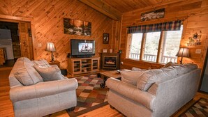 A cozy cabin interior with two sofas, a fireplace, a television, and wooden walls.
