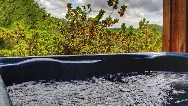 A hot tub with a view of lush greenery and a cloudy sky.