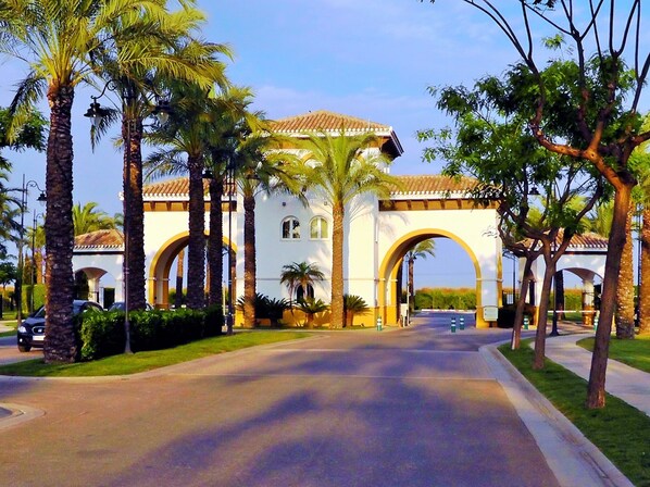 A white building with arched entrances, surrounded by palm trees and a paved road.