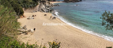 A sandy beach with rocky cliffs and clear blue water.