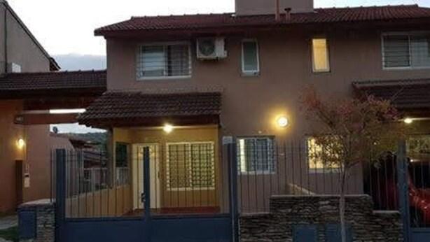 Una casa de dos pisos con base de piedra, techo de tejas y entrada protegida por una reja.