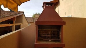 Una estructura de parrilla roja al aire libre con interior de ladrillo, adosada a un edificio con techo de tejas.