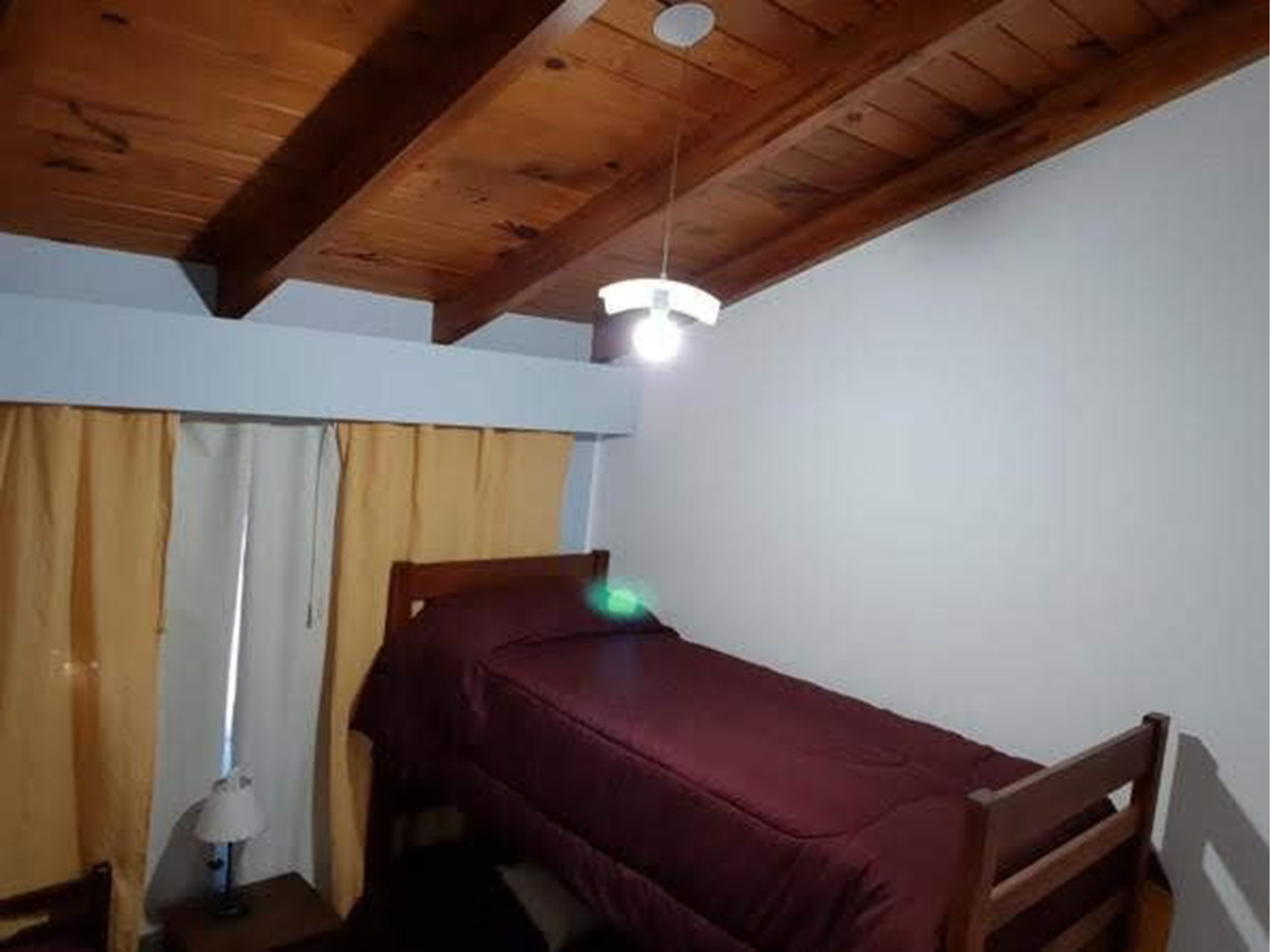 Una habitación pequeña con cama individual, techo de madera y una cama sencilla.