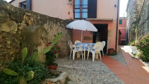 Uma área de estar acolhedora ao ar livre, com mesa, cadeiras, um guarda-sol branco e uma planta cacto.