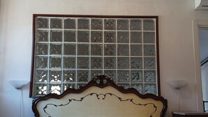 Quarto com cama, uma janela grande com painéis de vidro decorativos e duas luminárias fixadas na parede.
