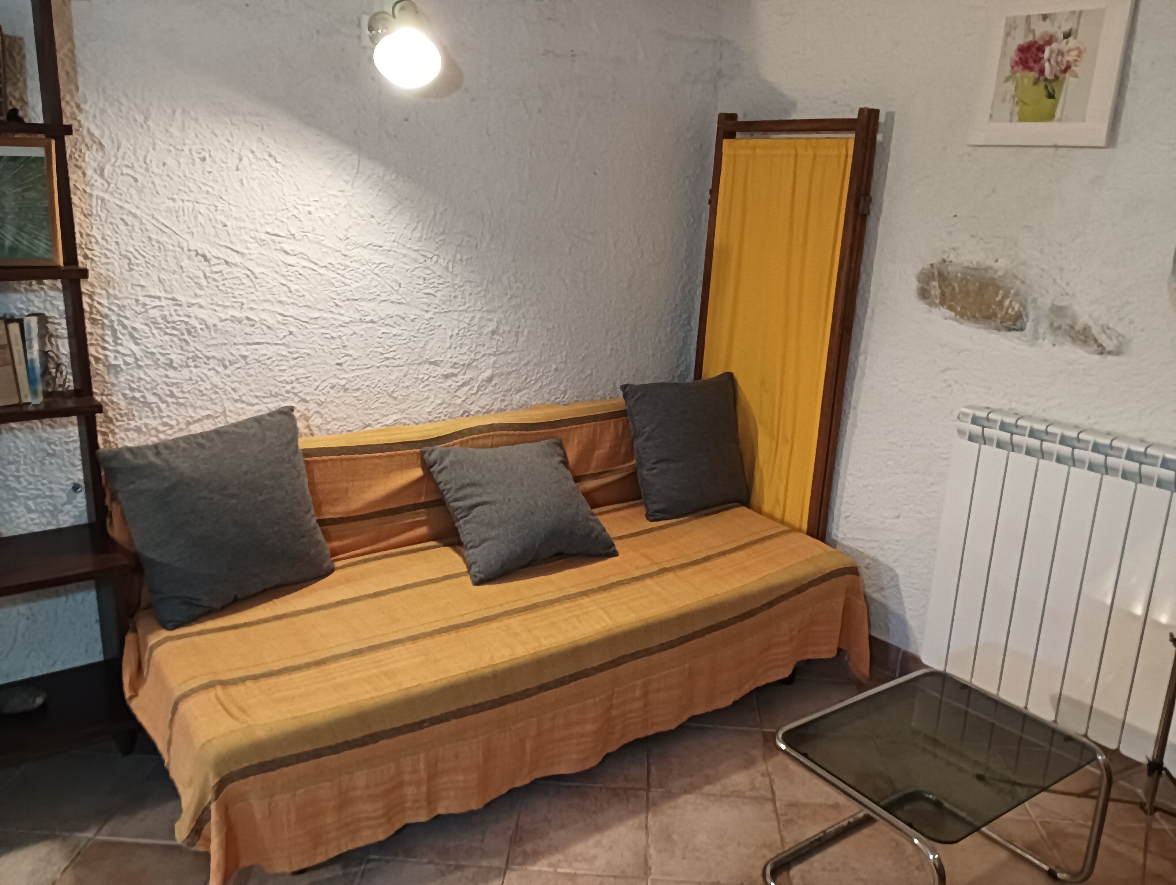 Una habitación pequeña y acogedora con una cama individual, una mesita de noche, un radiador y una estantería.