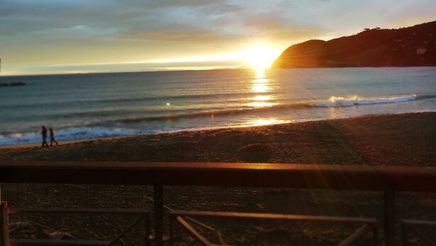 Uma praia com pôr do sol, ondas e uma colina ao longe.