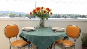 Ein Tisch für zwei, gedeckt mit einer grünen Tischdecke, zwei Stühle, eine Vase mit Blumen und Blick auf Bäume und Hügel.