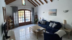 A living room with a blue sofa, a wooden coffee table, and a bookshelf. There is a stained glass window above the door and a painting on the wall.