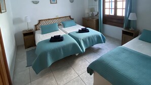 A bedroom with two beds, a window with curtains, bedside lamps, and a tiled floor.