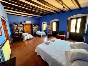 Quarto com uma cama grande, duas mesas de cabeceira, uma cadeira, uma estante e uma porta com janela.