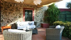 Eine Terrasse mit Steinmauern, Korbmöbeln, einem weißen Sofa und einem Tisch unter einer Markise.