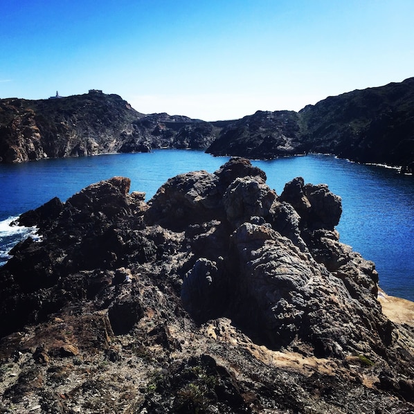 Une côte rocheuse bordée d’une mer d’un bleu limpide, avec un phare visible au loin.